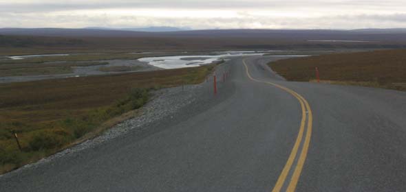 Paved portion of Dalton Highway south of Deadhorse, facing northbound, with small lake along left side of road
