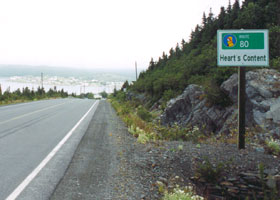 Heart's Content village sign, including small Baccalieu Trail marker, with village far in background