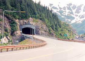 Two-lane highway tunnel under Begich Peak, west portal, with snowplow guides on the approach road